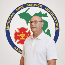 Man in a white polo standing in front of the Michigan Fire Service Instructors Association logo.
