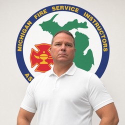 Portrait of a man in a white polo shirt standing in front of a circular Michigan Fire Service Instructors emblem in a professional setting.