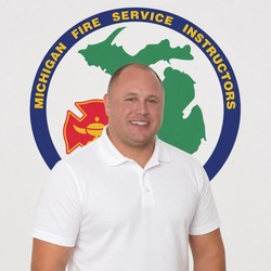 Man wearing a white polo shirt standing in front of a circular Michigan Fire Service Instructors logo.