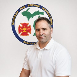 Portrait of a man in a white polo standing in front of a Michigan Fire Service Instructors Association emblem backdrop.