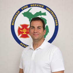 Portrait of a man in a white polo shirt standing in front of a circular Michigan Fire Service Instructors Association logo.