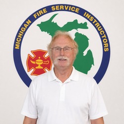 Man in a white polo standing in front of a Michigan Fire Service Instructors emblem on the wall.