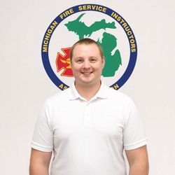 Portrait of a smiling man in a white polo shirt standing in front of a circular emblem for a Michigan fire service instructors association.