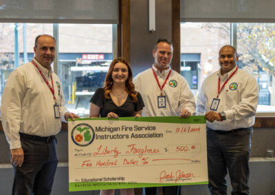 Four adults pose with a large ceremonial check from the Michigan Fire Service Instructors Association in an office setting.