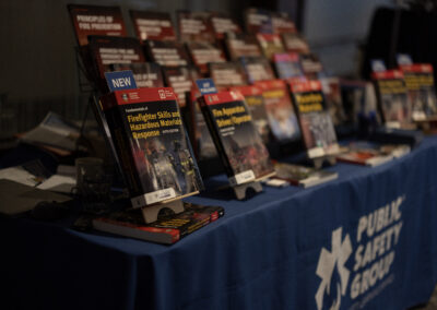 Display of firefighter training books on a table, including 'Fundamentals of Firefighter Skills and Hazardous Materials Response' with a blue NEW sign in front.